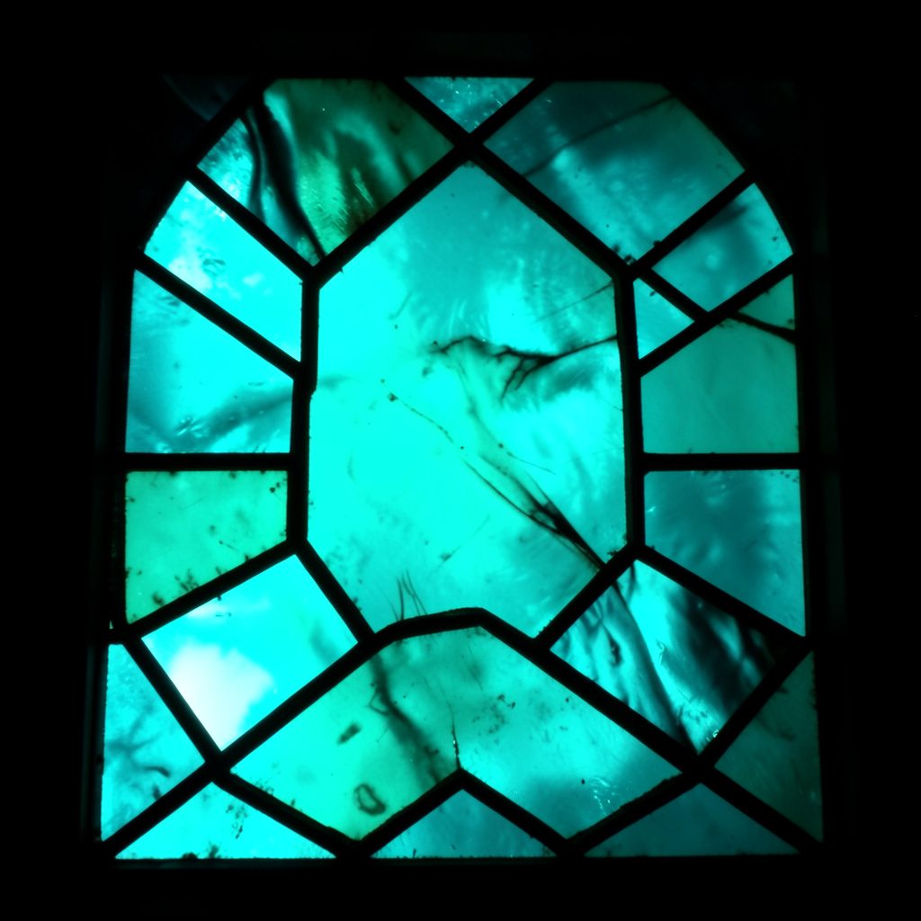 Abstract stained-glass composition with bold leaded segments in deep teal, soft white, and warm amber, casting a contemplative mood.